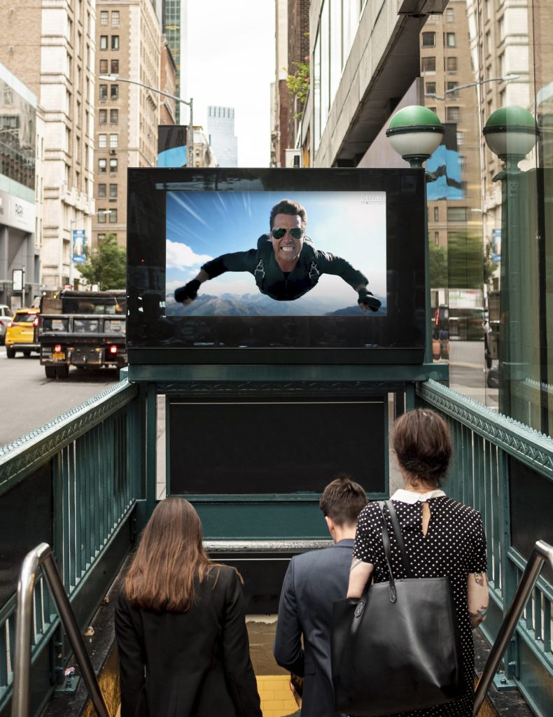 An AI video flashed on a screen by the entrance of a subway.