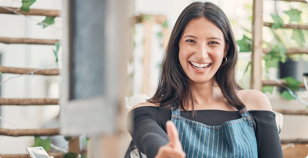 A woman gladly showing a thumbs up while wearing an apron.