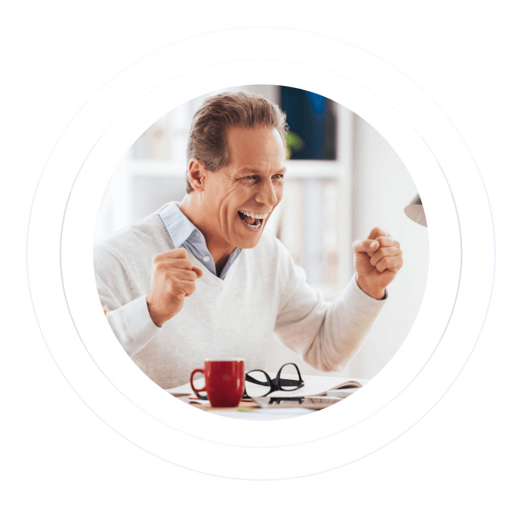 A man wearing a white sweater on top of his shirt is cheering in joy while gazing at his laptop screen.